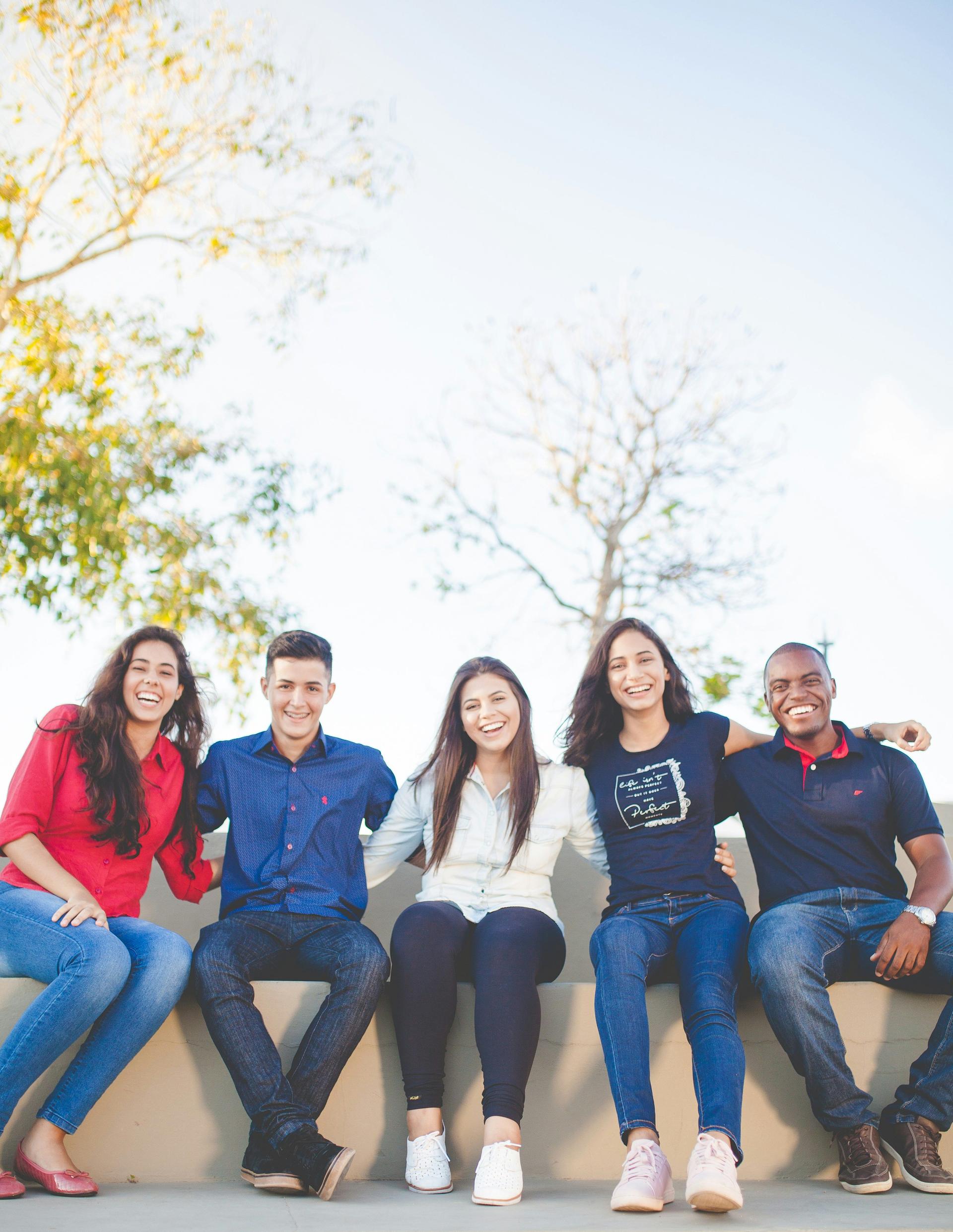 A diverse group of young individuals casually seated on a brick wall, enjoying each other's company in a relaxed setting.