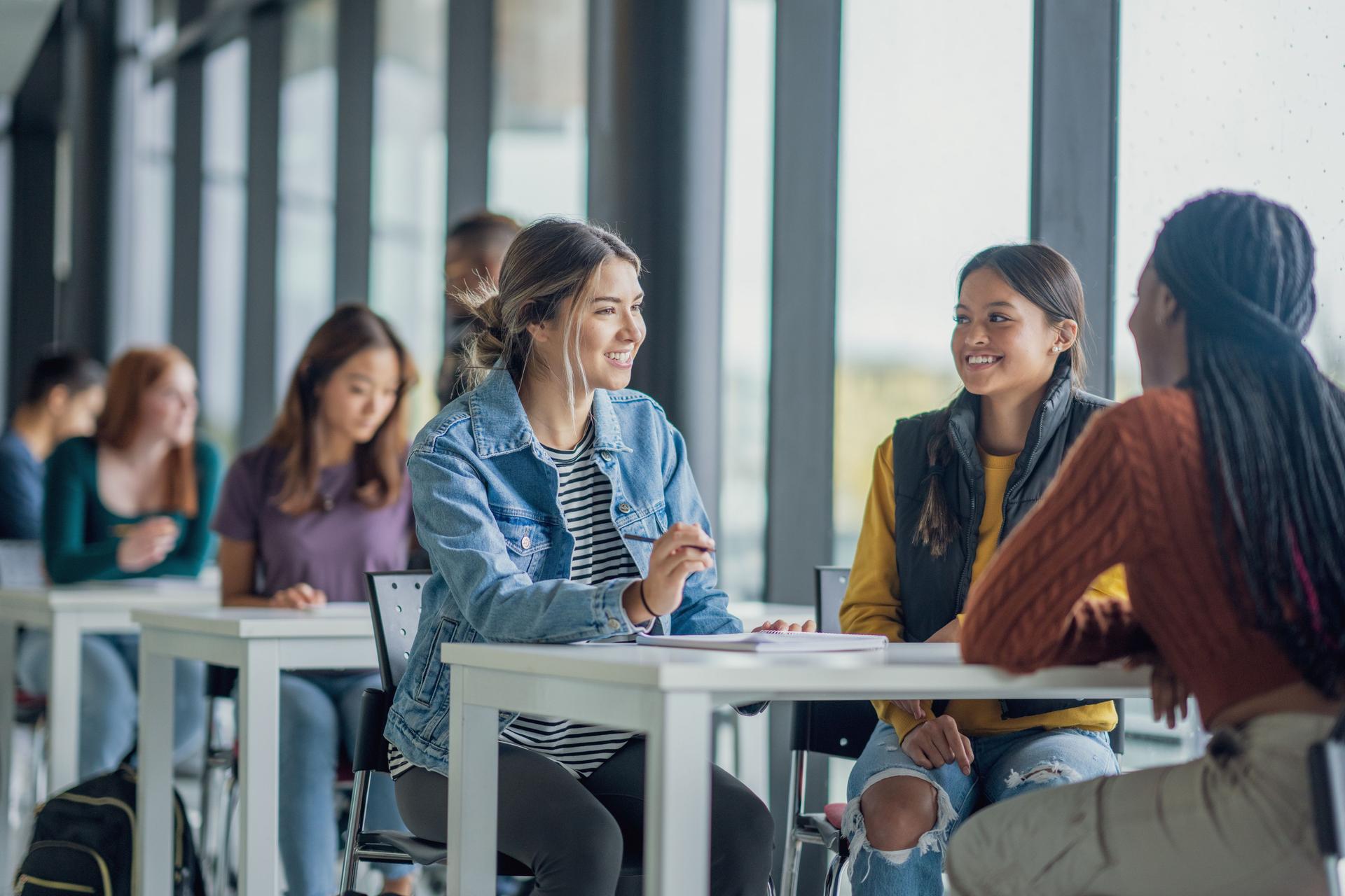 Students gathered at tables in a classroom, actively studying and collaborating 