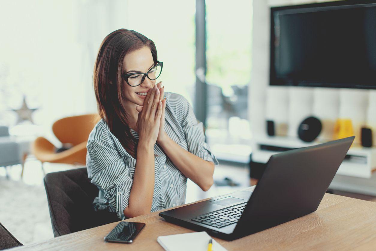 A joyful woman, immersed in her studies, sits at a table with a laptop, showcasing her commitment.