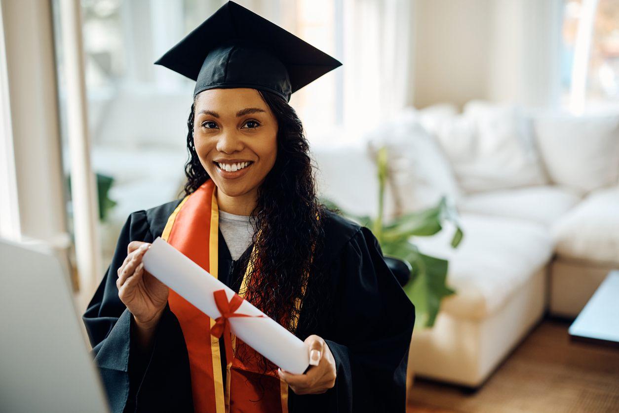 A woman in a graduation gown proudly holds her diploma, symbolizing her academic achievement and success.