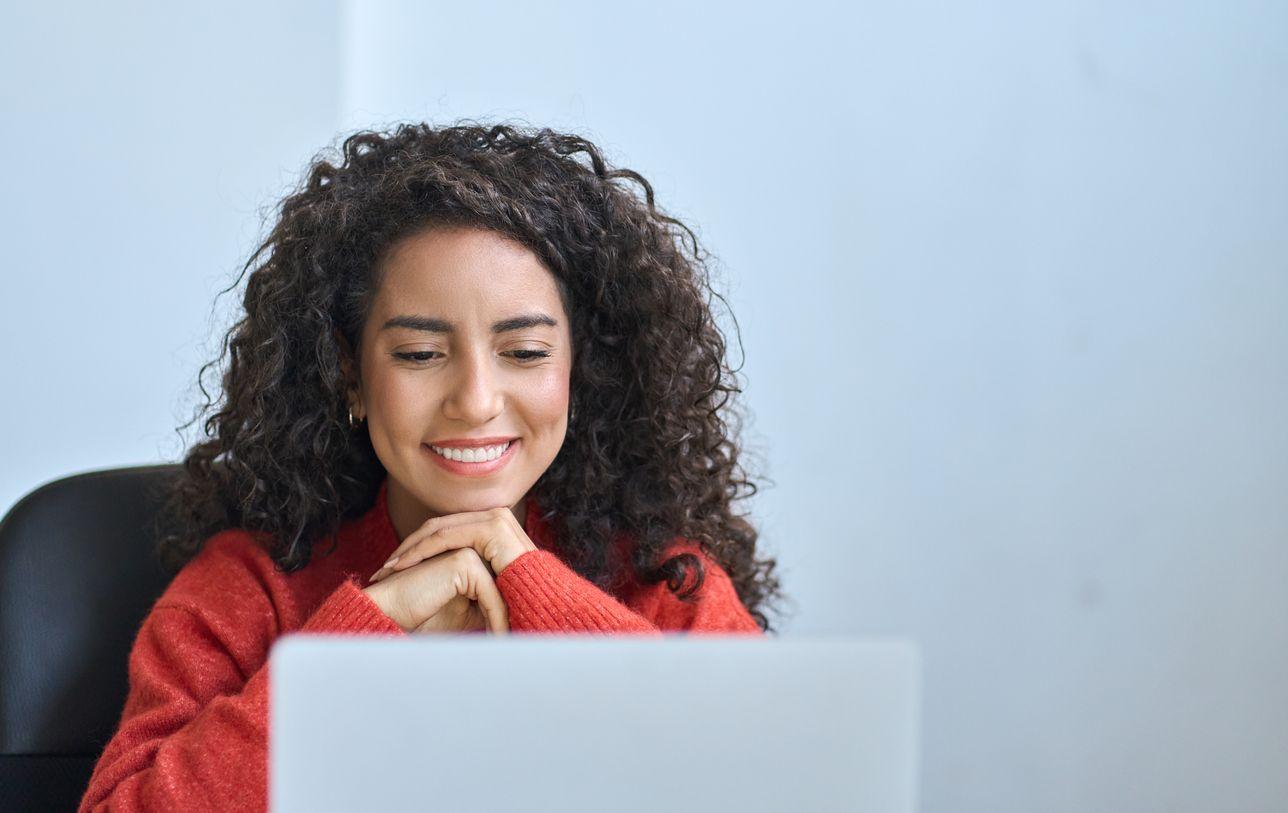 A woman with curly hair is seated at a desk, focused on her laptop, creating a productive work environment.