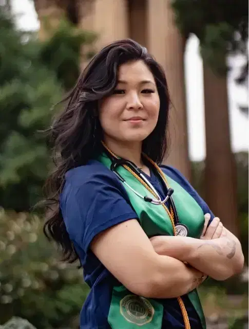 Confident healthcare professional in scrubs with a stethoscope, standing outdoors with arms crossed.