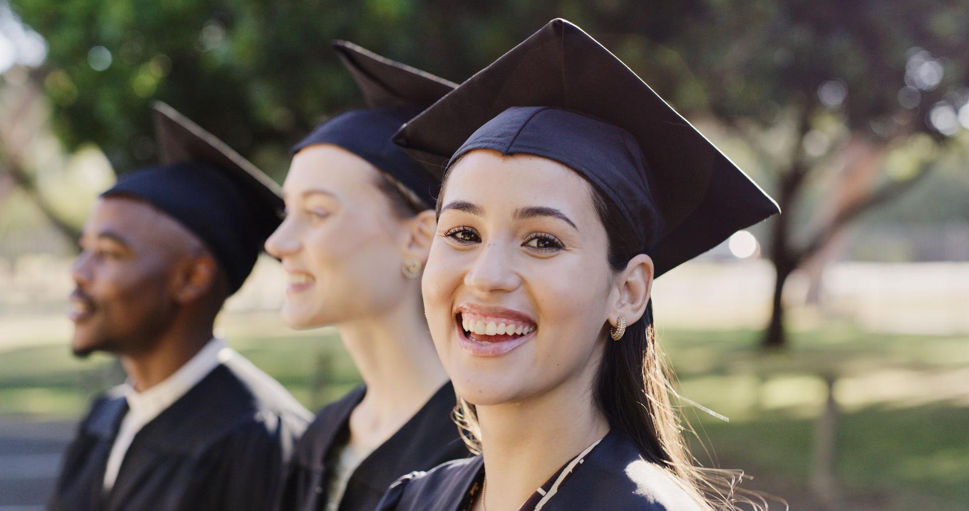 Graduates in caps and gowns smile joyfully as they stand together, marking a significant milestone in their education.