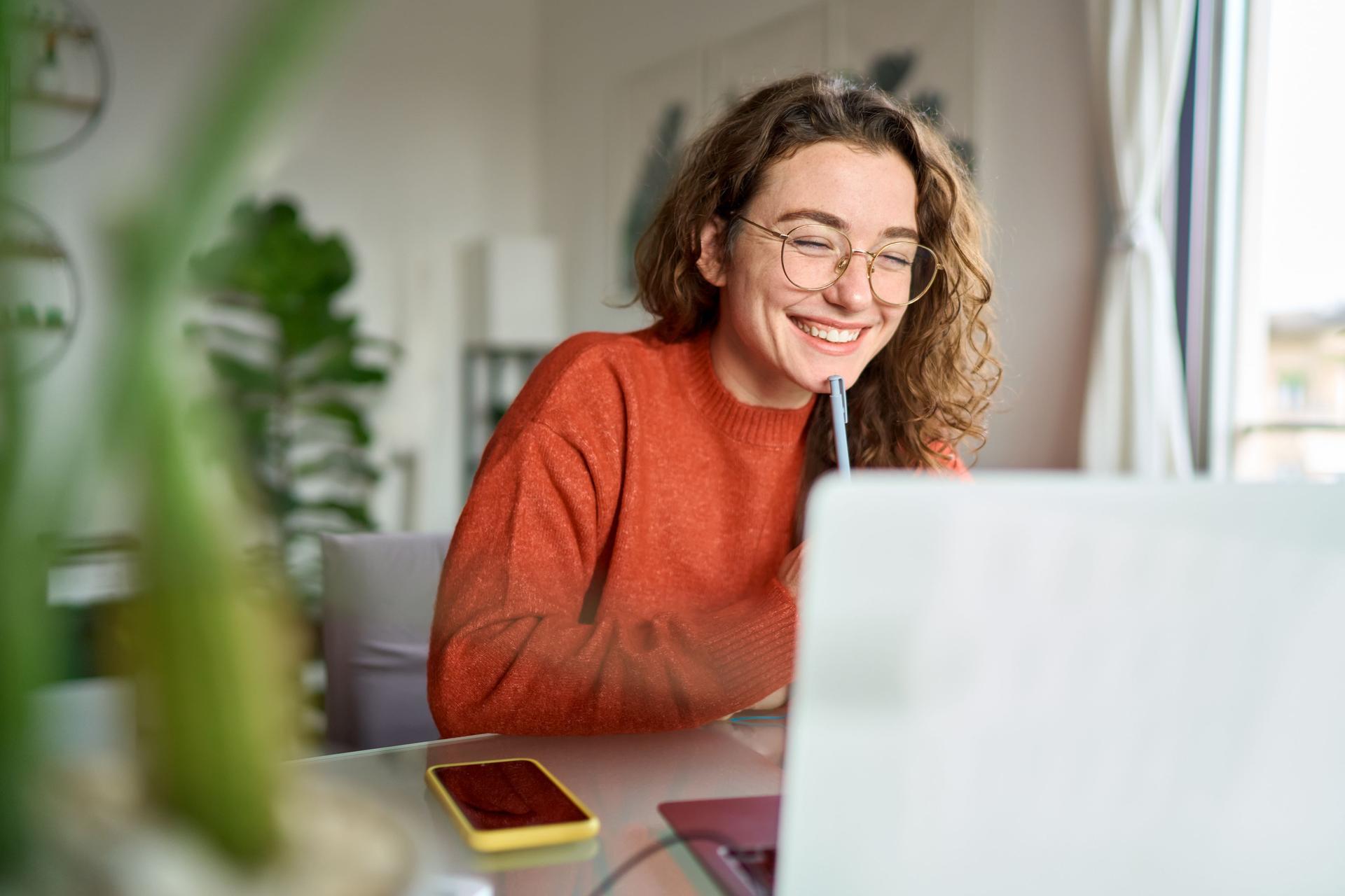  A student happily engages with her laptop, participating in remote learning in her home environment.