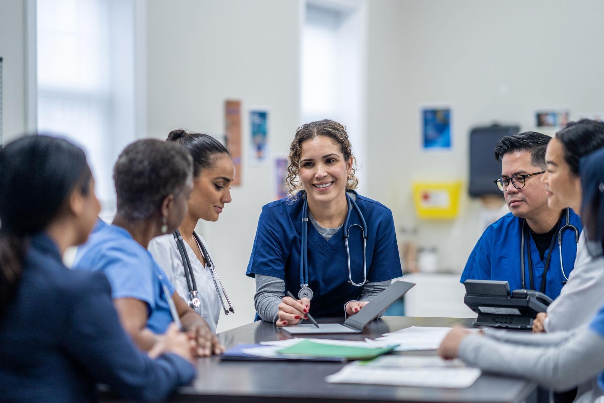 A group of nurses engaged in discussion while seated around a table, showcasing teamwork and collaboration.