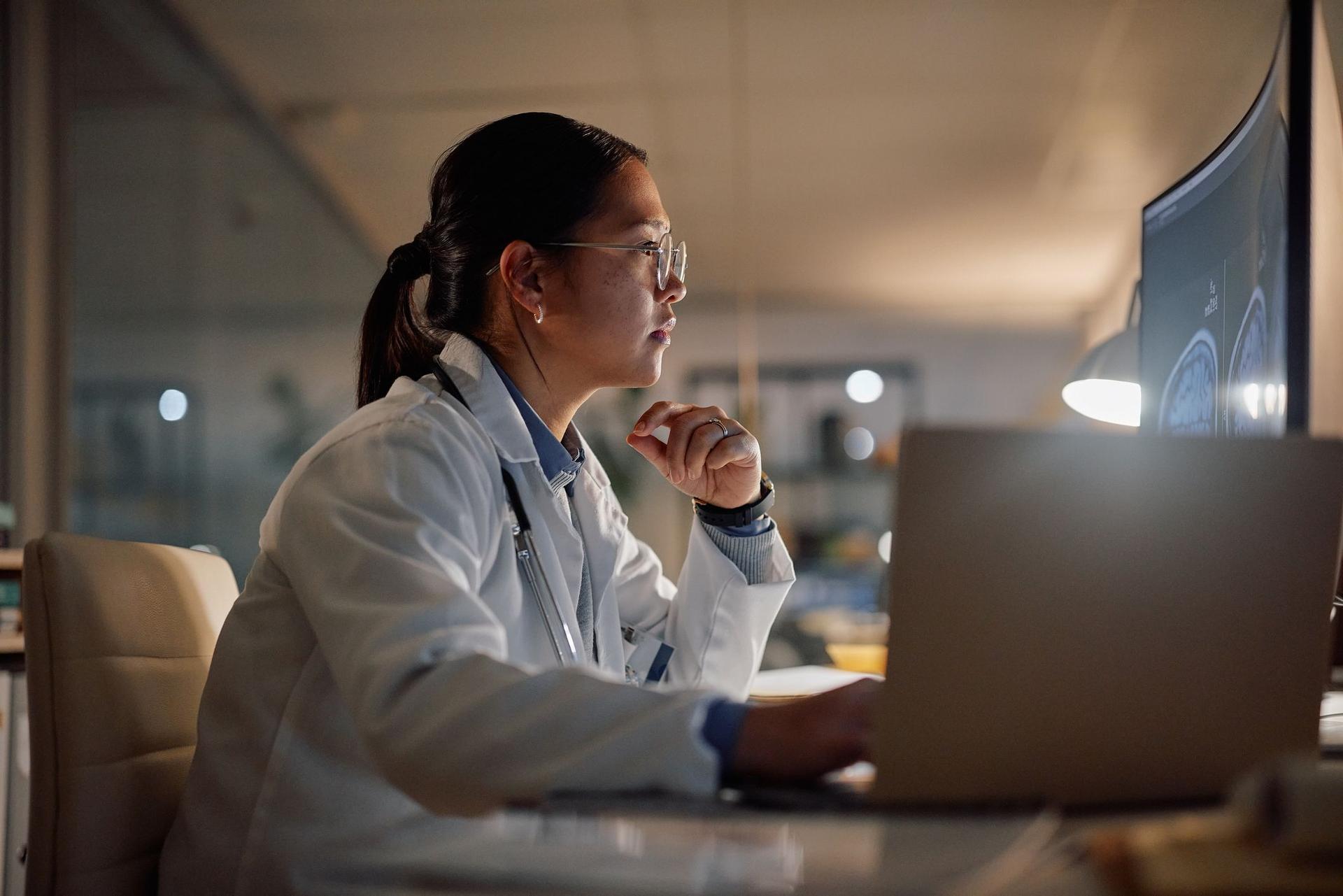 A female doctor in a lab coat analyzes information displayed on a computer screen.