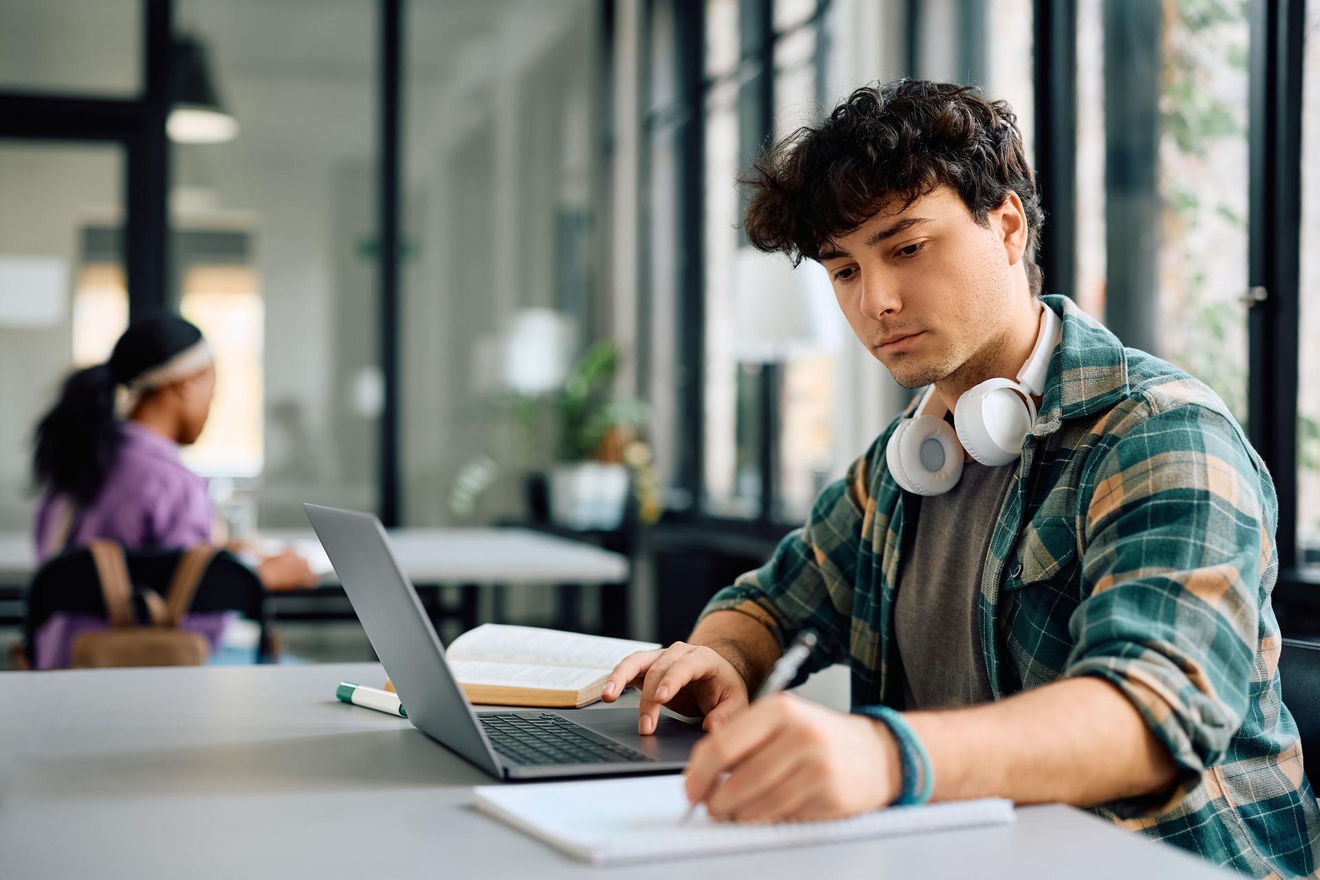 A man wearing headphones is focused on his laptop, engaged in work or a project.