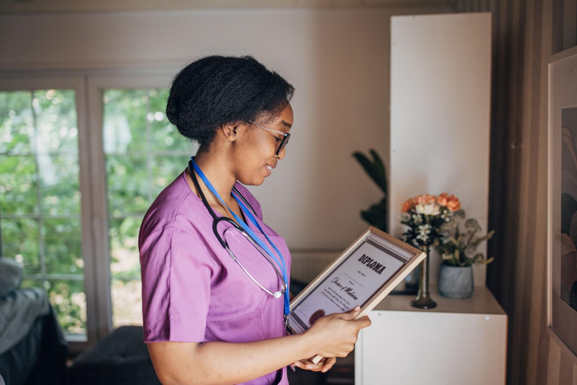 A nurse in a purple shirt examins her degree diploma, showcasing her professional dedication