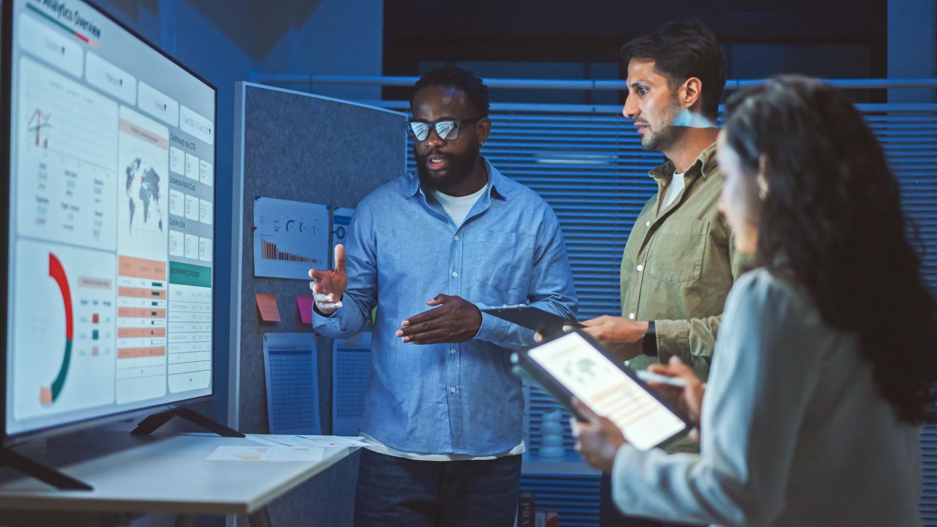 group of three people focused on a presentation displayed on a screen, engaged in a collaborative environment.