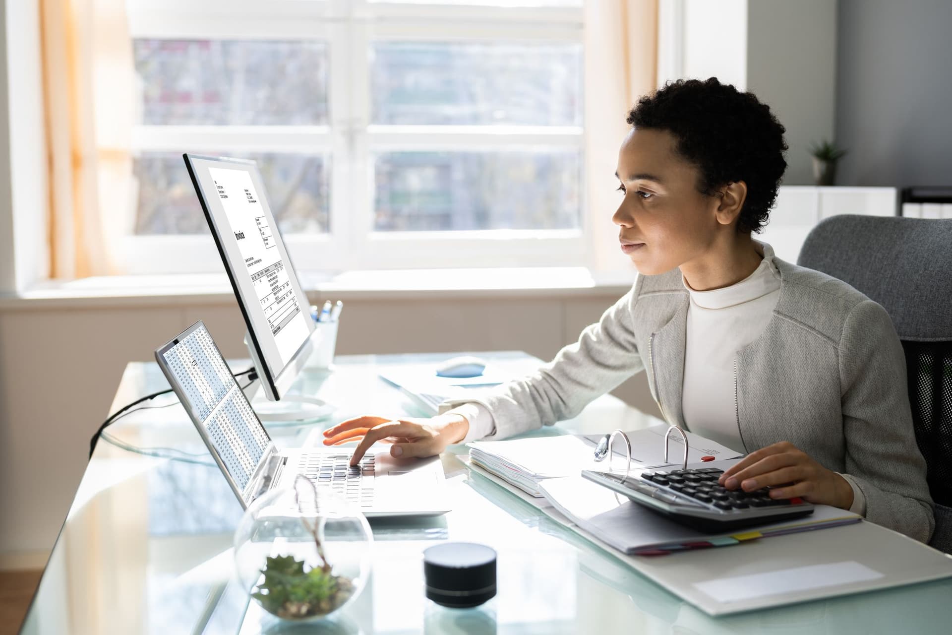 A woman engaged in her work on a laptop, with a calculator in use beside her.