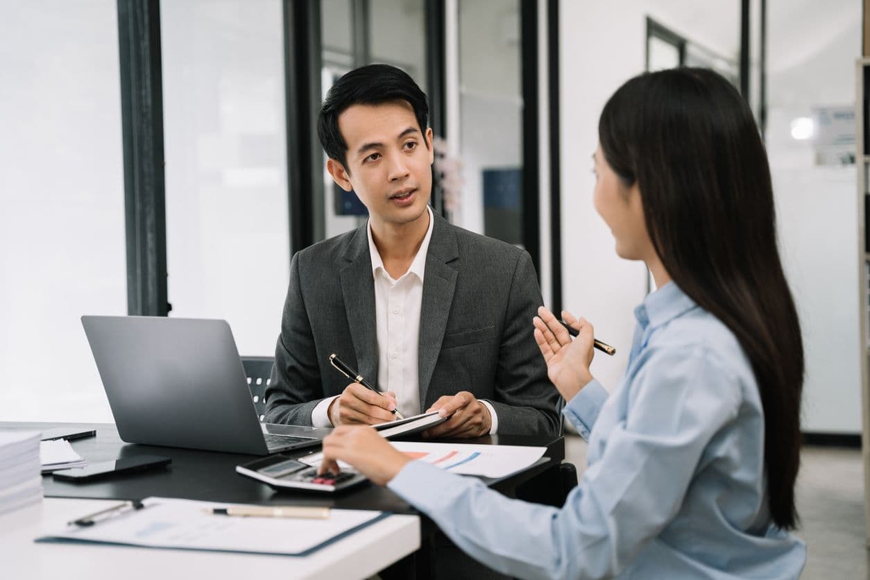 A man and woman dressed in business attire discussing ideas in an office environment.