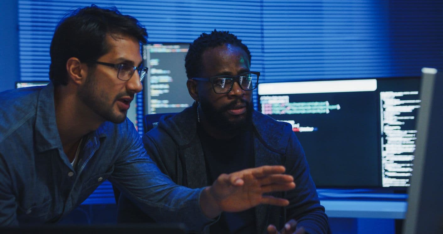 Two men discussing cybersecurity while analyzing data on a computer screen.