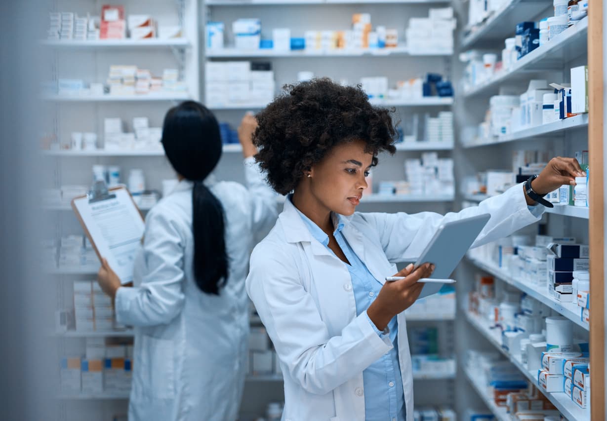 A pharmacist standing behind the counter in a pharmacy, surrounded by shelves of medication and health products.