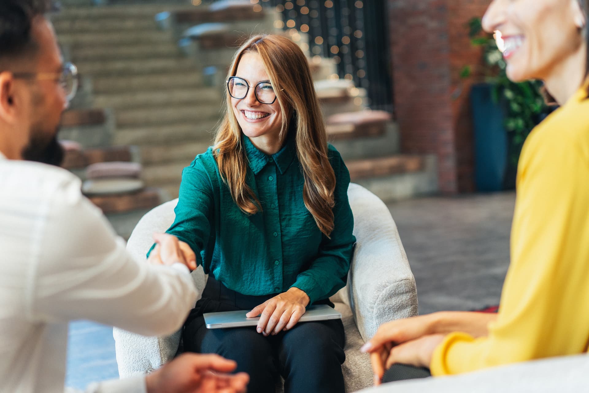A woman shakes hands in a professional setting, smiling and engaging in conversation.