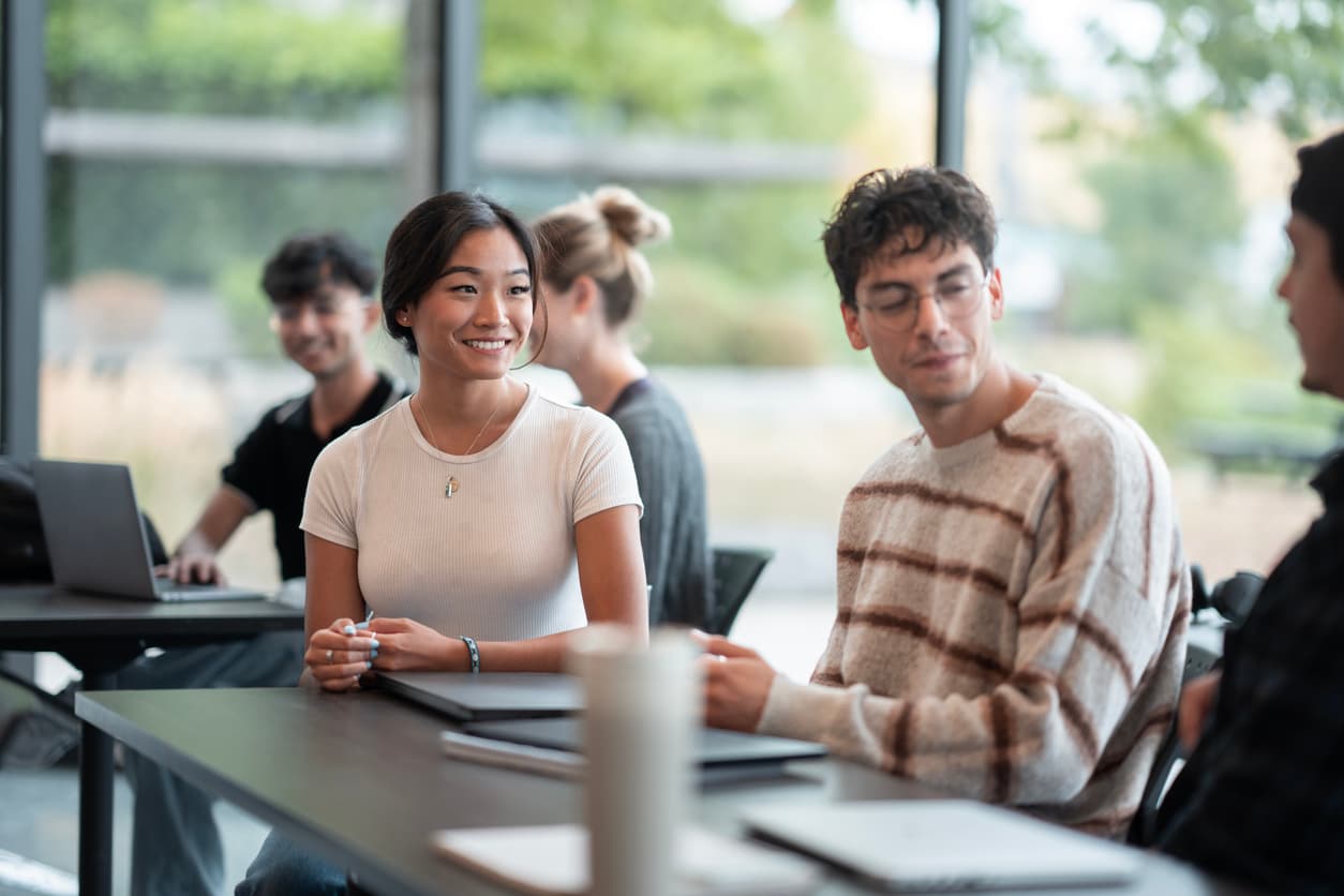 A group of students engaged in discussion while sitting around a table in a classroom setting.