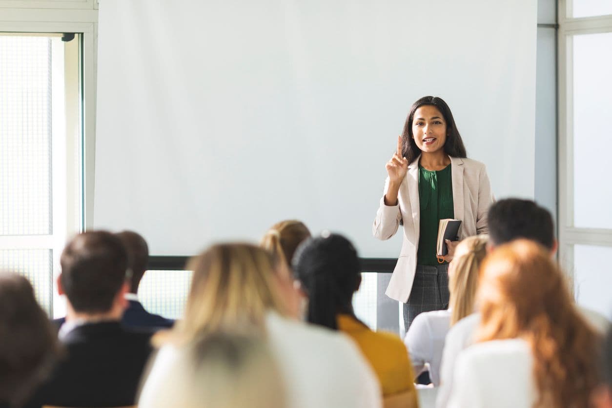 A woman delivering an educational presentation to an attentive audience in a classroom.