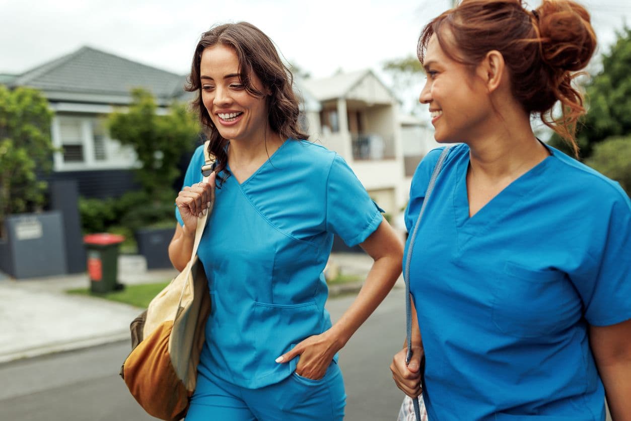 Two women in nursing scrubs walking side by side down a city street.