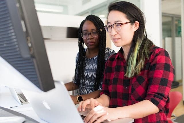 IT manager workin at a desktop computer with a colleague next to them