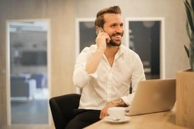 Man at a coffee shop talking on the phone with laptop in front of him