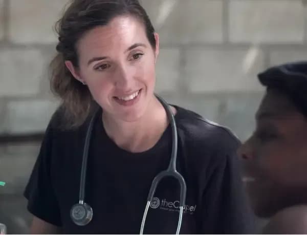 A healthcare professional wearing a black shirt and a stethoscope around her neck smiling and talking to a patient.