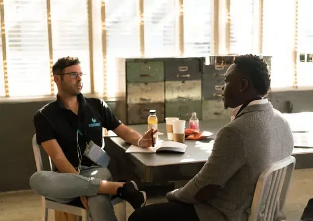 A career advisor sits across from a client in a casual office setting, engaged in a discussion. The scene conveys a supportive and professional atmosphere for career guidance.