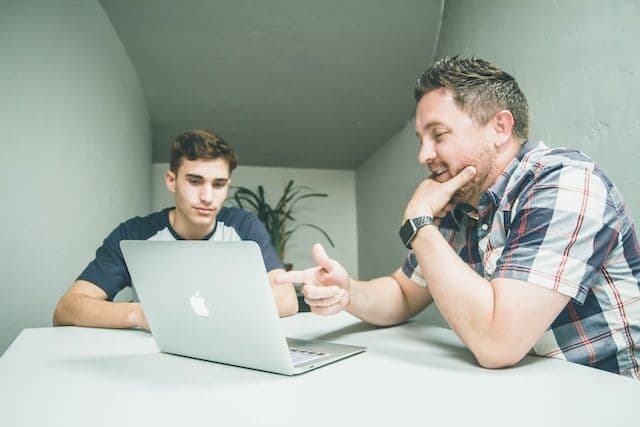 A senior data analyst pointing to a laptop seated next to a colleague