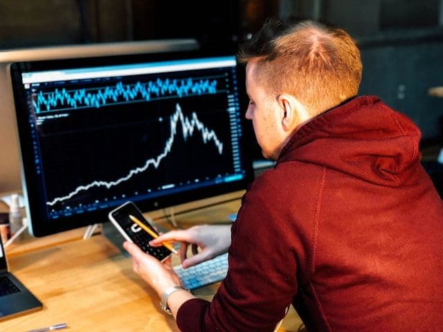 A financial analyst interacting with a phone in front of monitor displaying a financial graph