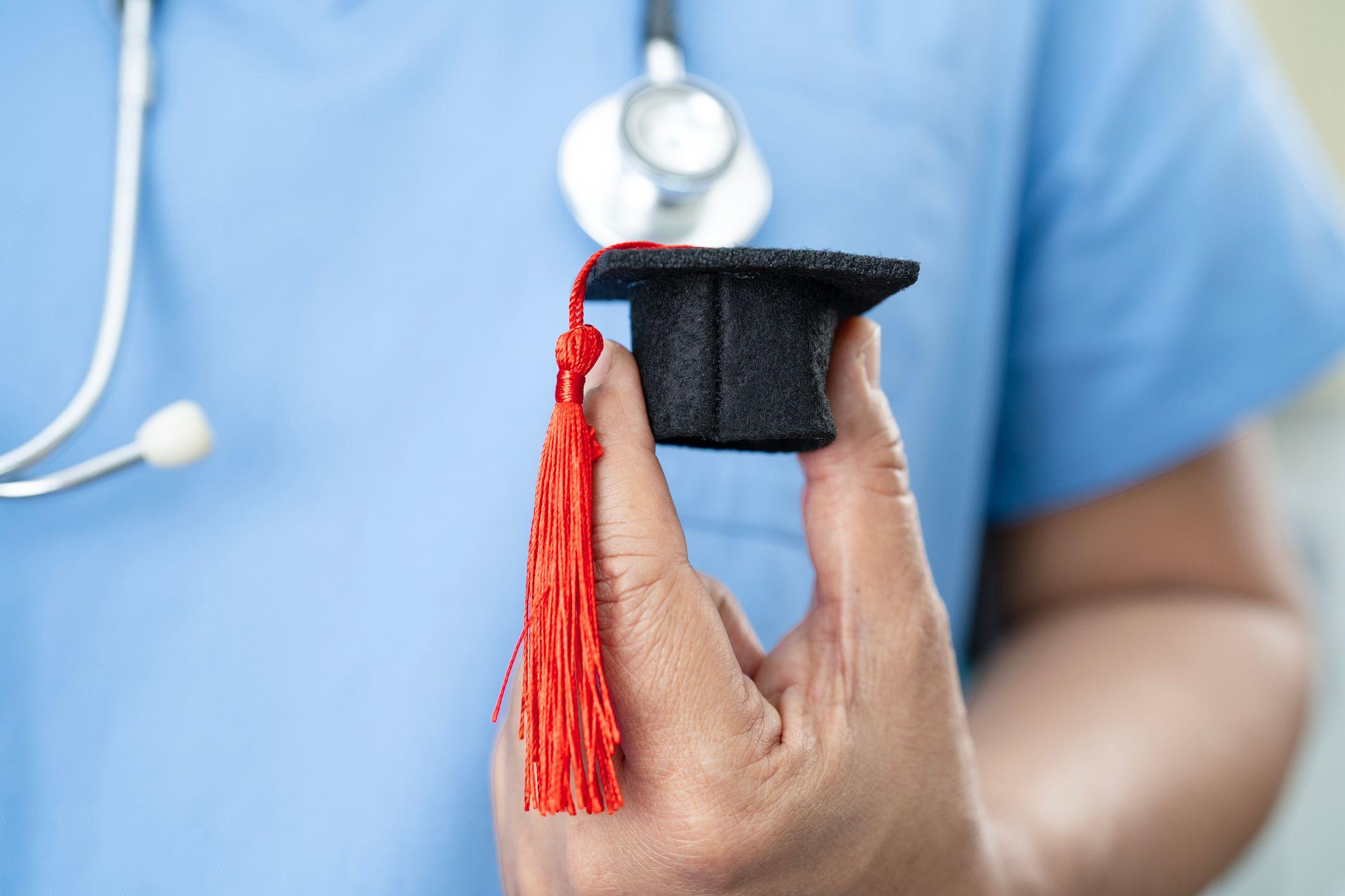 A nurse proudly holds a graduation cap with a tassel, symbolizing her achievement in the nursing profession.