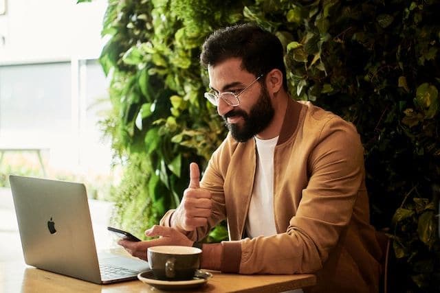 Product manager manipulating a mobile device while working in front of a laptop