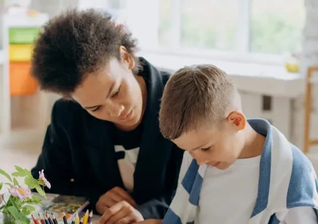 A special education teacher assists a young boy with his work in a classroom. The teacher provides individualized support, fostering a nurturing and focused learning environment.