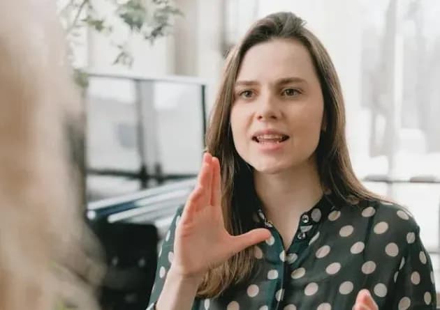 A teacher using sign language to communicate with a student. The teacher's expressive gestures highlight her dedication to supporting individuals with hearing or sight impairments.