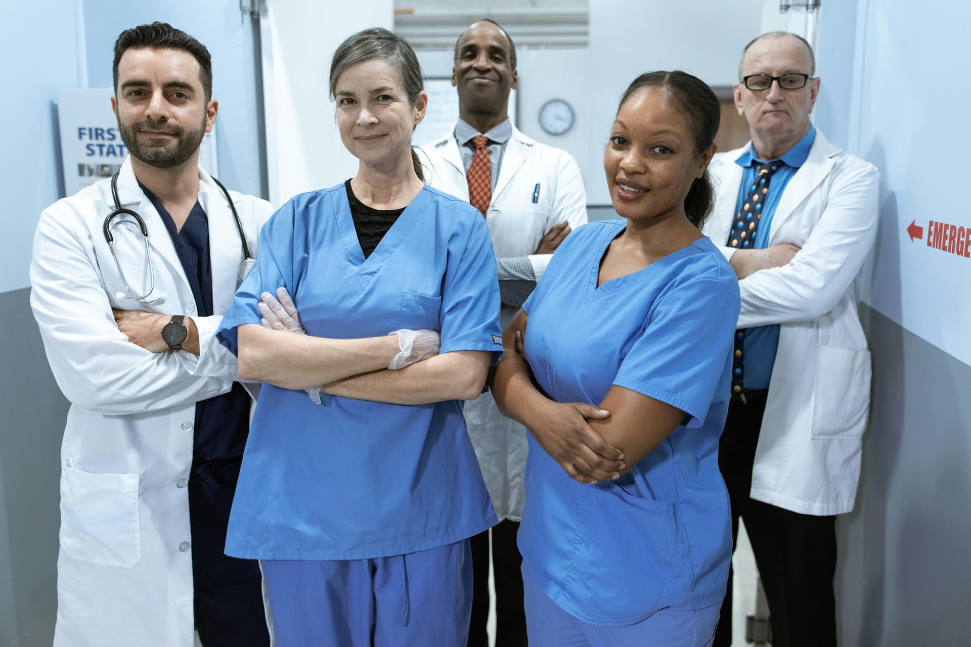 A group of five healthcare professionals, consisting of doctors and nurses, stands together in a hospital hallway, looking at the camera with confident expressions.