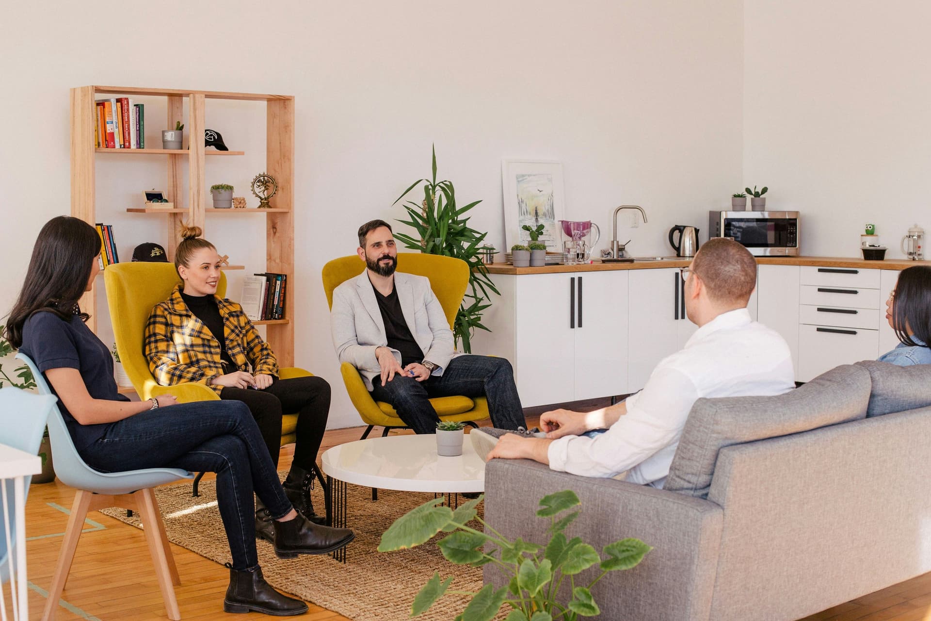 Five people sitting in a casual meeting room, talking.
