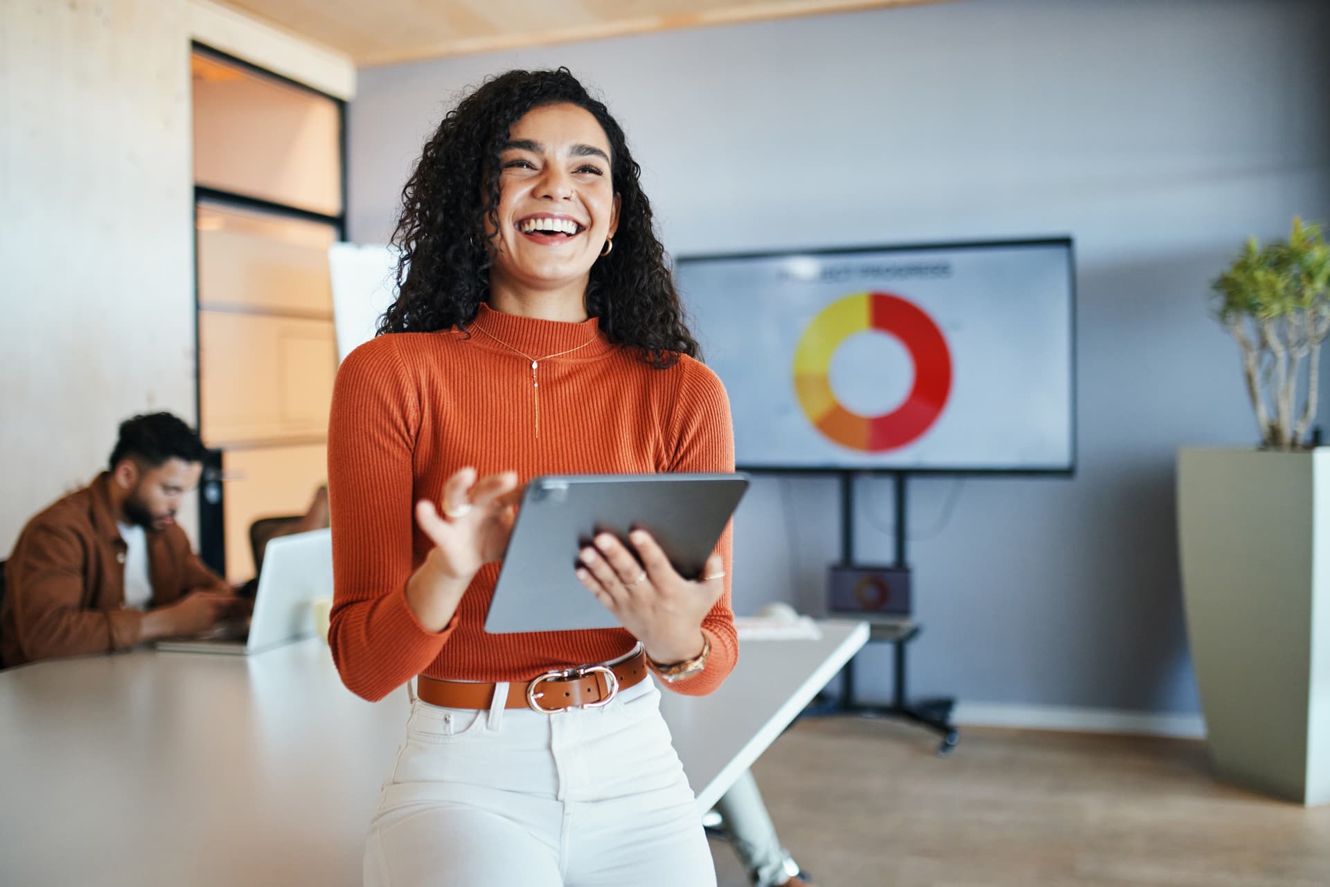 A cheerful woman is smiling while holding a tablet computer, reflecting a sense of joy and engagement.