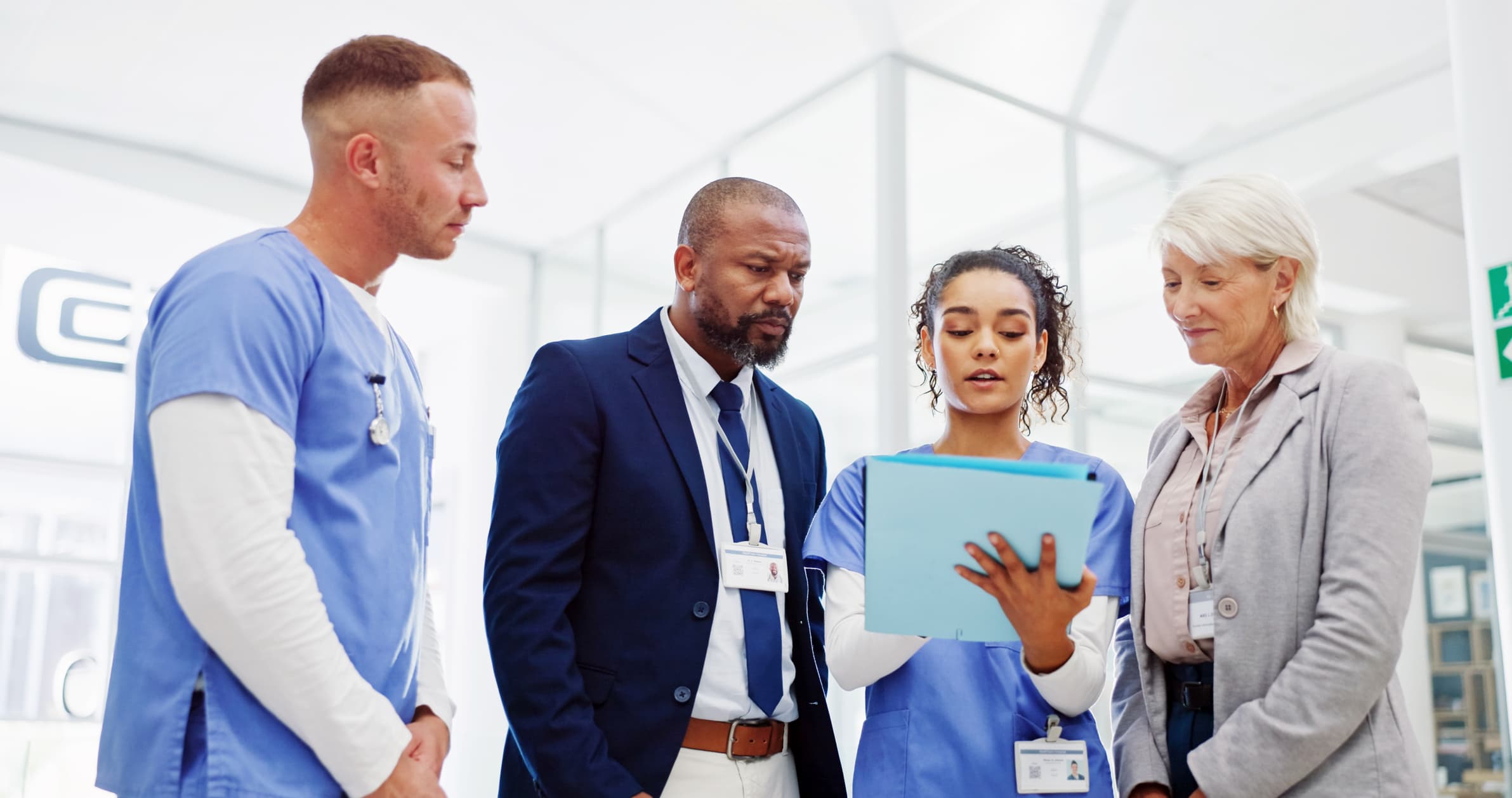 A group of healthcare professionals in scrubs examining a tablet together, engaged in discussion.