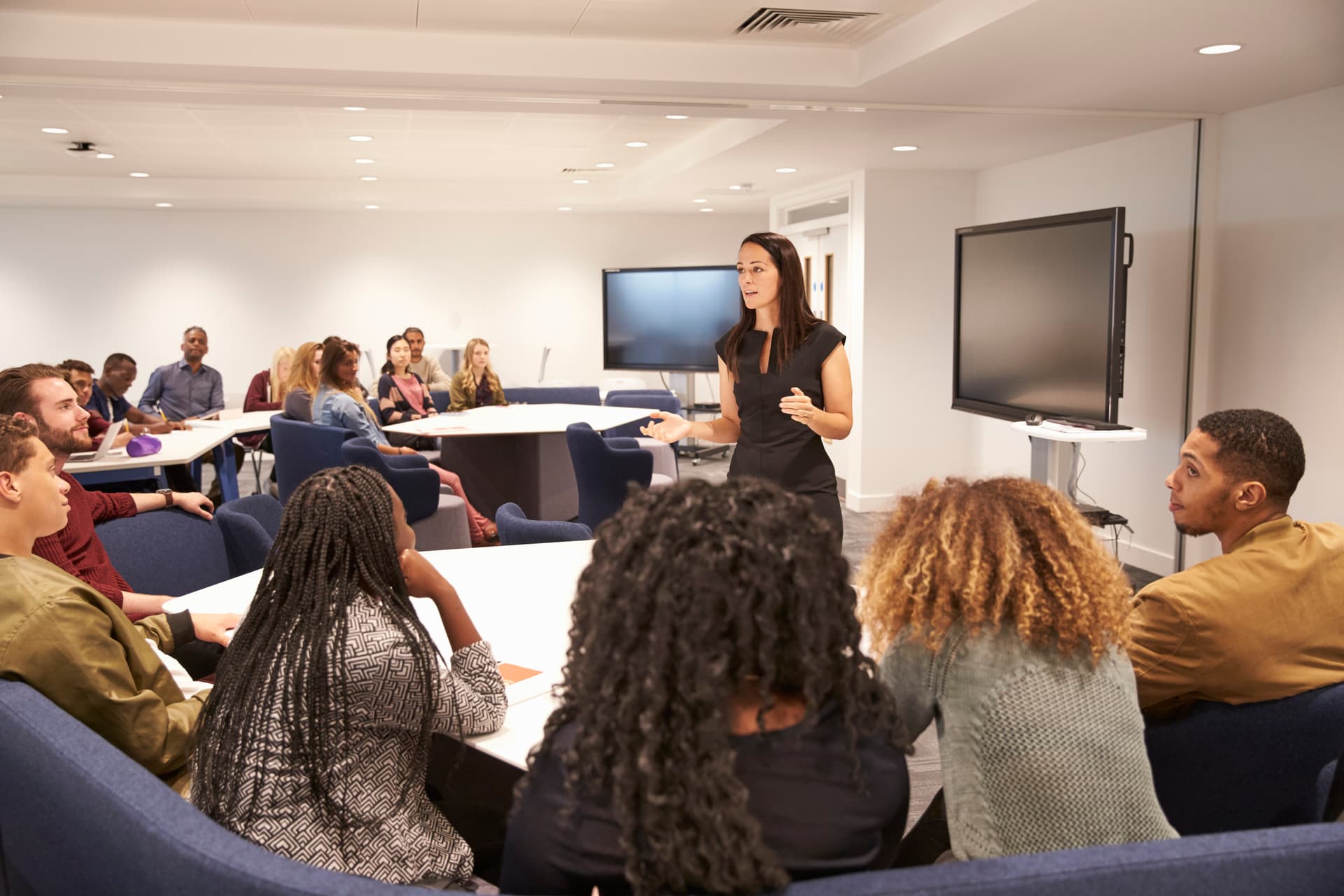 A woman stands before a group, delivering a presentation and interacting with her audience.